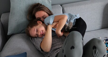Elder sister tickles young four five year old brother on sofa at home. Warm and close family...