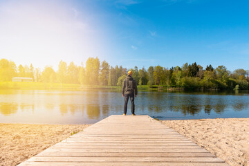 Young man standing alone on edge of wooden footbridge and staring at lake