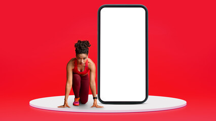 Serious young black slim woman athlete in sportswear and headphones ready to run at start