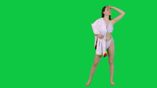 Model in a bikini and a towel looking of a spot and walking away in front of a green screen