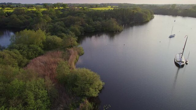 Sideways aerial footage of Wroxham Broad, a body of water in the Norfolk Broads national park. Captured on a bright summer evening just before the sun started to set