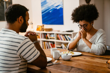 Young couple praying during lunch while sitting in kitchen