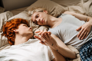 Obraz na płótnie Canvas Gay couple holding hands while laying on bed