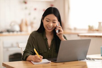 Cheerful asian woman entrepreneur working from home, using laptop, smartphone