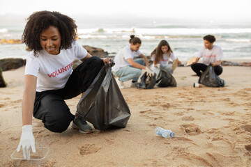 Positive young multiracial people volunteers in rubber gloves and african american lady with trash...