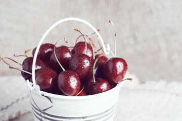 Small white bucket full of red cherries on a linen cloth background.