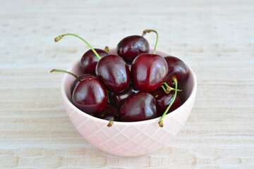 A heap of cherries in a pink bowl isolated on the beige background, copy space