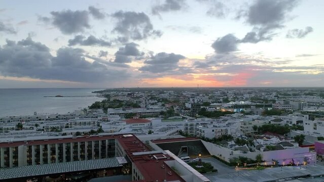 Aerial view of a cityscape by the coast, with built structures, rolling clouds and endless horizon on magic hour in Playa del Carmen, Mexico.
