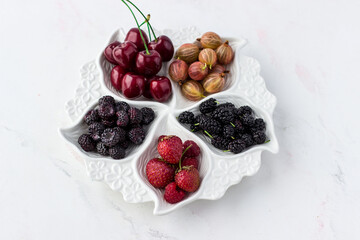 Berry plate on a white background. Strawberries, gooseberries, cherries, raspberries and mulberries