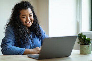 Happy young chubby woman working from home, using laptop