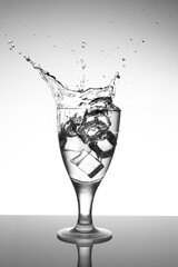Chilled clear liquid splashing from a wine glass after ice cubes are dropped in. Splash-free table and white background.