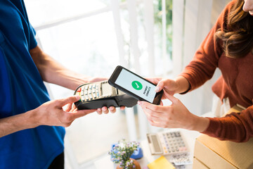 Woman paying bill through smartphone using contactless payment technology. Satisfied customer paying through mobile phone using NFC technology. Closeup hands of mobile payment at mobile handheld POS.