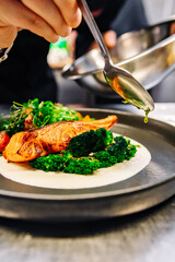 chef hand preparing a gourmet salmon steak with broccoli on restaurant kitchen