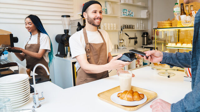 Smiling male barista using card swipe machine to pay in coffee shop