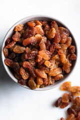 Raisins in ceramic bowl on marble background. Dried grapes on white background. Top view.