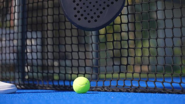 Closeup of a padel player picking up the racket and the ball by the net of the court and starting playing.