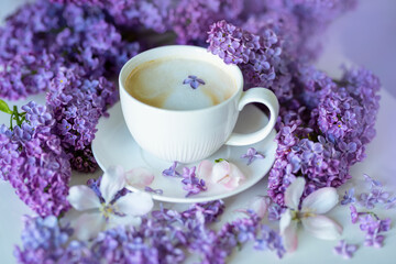 Obraz na płótnie Canvas Delicate spring flowers of lilac and jasmine and a cup of coffee with milk. Delicate morning coffee with a wonderful spring-summer mood. Soft selective artistic focus.