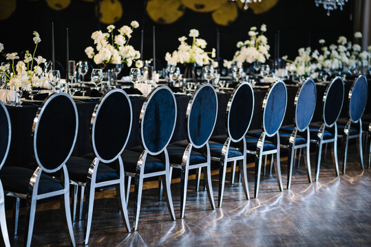 Chairs for guests. Banquet decoration in hall restaurant. Festive tables with flower composition on black tablecloth. Wedding set up, dinner table reception in area on party. Setting and interior.