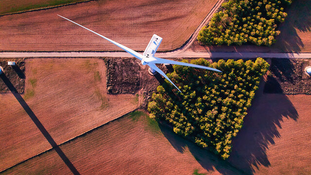 Aerial view (on top ofl) of a group of wind turbines in a row over an agricultural field at sunset. Close-up to a group of wind turbines spinning in a row in a wind farm, Spain 