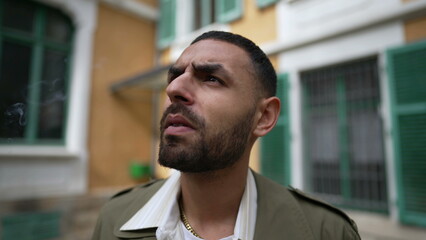 One pensive serious young Middle Eastern man smoking a cigarette outside with thoughtful expression. Tracking shot closeup face in motion while brooding