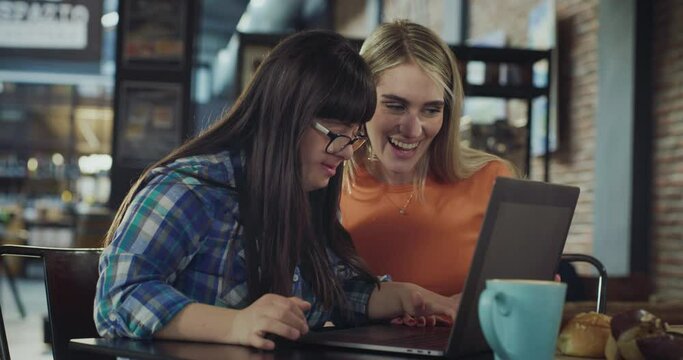 Portrait of Young Woman with Down Syndrome Learning New Skill on Laptop Computer with her Female Friend or Manager. She is Starting a New Job, Checking Inventory in a Local Cafe Business. Slow Motion