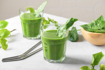 Healthy green smoothie with spinach, banana, and vegan milk in two glasses and fresh ingredients on light grey table. Detox, diet, healthy, vegetarian food concept
