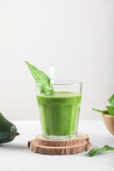 Healthy green smoothie with spinach, avocado, banana, and vegan milk in glass and fresh ingredients on light gray table