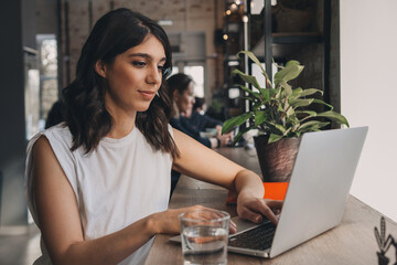 Attractive positive young woman using a laptop in a cafe.Remote work,blogging,business,...