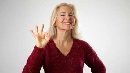 Smiling cheerful fascinating elderly gray-haired blonde woman lady 50s years old wears red sweater showing okay ok zero fingers gesture isolated on solid white background studio portrait