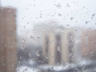 wet snow flakes on window glass in city apartment and view of city block on background