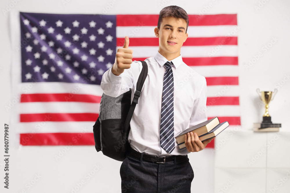 Wall mural teenage male student holding books and showing thumbs up in front of usa flag