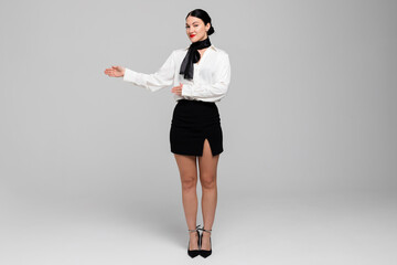 Portrait of an attractive young Stewardess. Charming, smiling air hostess in sensual uniform, gesturing, offering to come in. Isolated on white background.