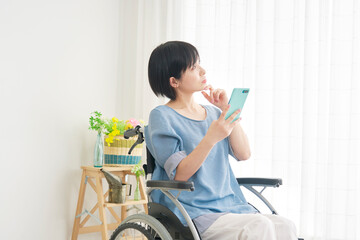 リビングでスマートフォンを使いながら考える車椅子に乗った女性
