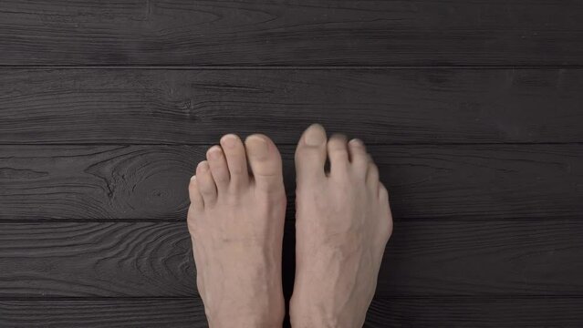Male feet with extremely long and terribly untrimmed nails on a black wooden background or floor. Close up, top view, point of view