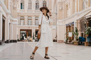 Gordijnen attractive woman walking in shopping street in Italy on vacation dressed in white summer fashion dress © mary_markevich