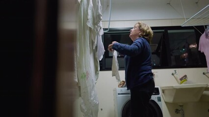 Senior woman tending to laundry on drying rack, a glimpse into daily life. Domestic routine scene of retired older lady at home. Candid and authentic