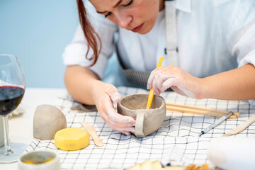Crop woman using stick to make clay cup smooth