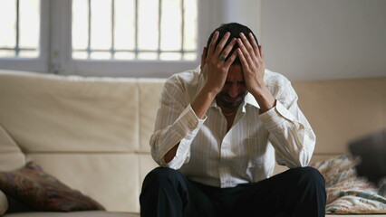 Dramatic young man feeling distraught and stressed from emotional pressure. Frustrated male person sitting at home hitting couch with hand acting aggressive