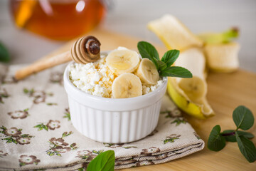 crumbly organic cottage cheese with honey and bananas in a ceramic bowl
