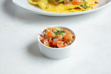 A view of a ceramic condiment cup of pico de gallo salsa.