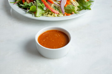 A view of a spicy red Asian dressing in a white ceramic condiment cup.