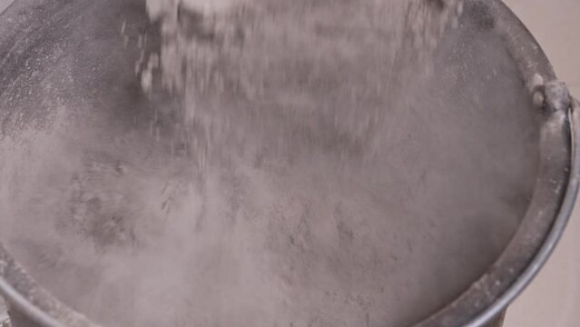 The process of pouring dry cement into a construction bucket in slow motion. Construction dry cement for concrete mix close-up.