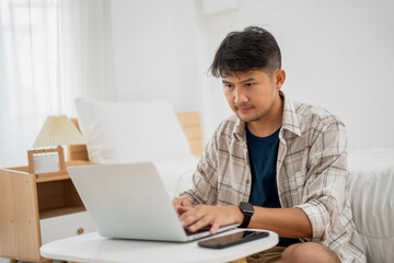 A Young Man Working on his Laptop Asian Male Freelance Businessman using Laptop Computer to Work Online Searching for Technical Information on the Internet sitting at a Desk.