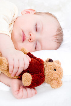 cute little girl sleeping with teddy bear on the white blanket