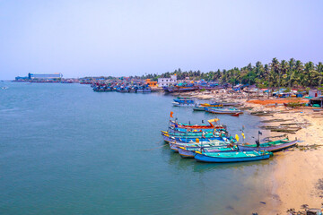 the boats standing near waves of ocean with jungle and white sky