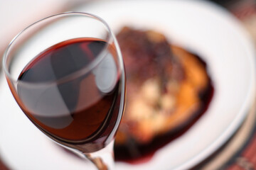 Red wine in a glass with shallow depth of field and soft focus, in front of a meal with a rich, red wine sauce.
