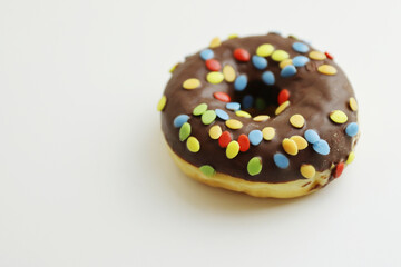 One Donut glazed with chocolate and colorful smarties isolated on white background. doughnut with colorful chocolate nibble on top. Side view. Copy space.