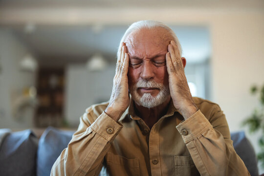 Shot of a senior man suffering from a headache at home. Unpleasant pain. Sad unhappy handsome senior man sitting on the sofa while having headache