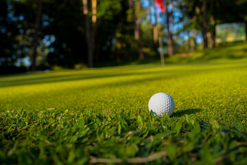 Golf ball is on a green lawn in a beautiful golf course with morning sunshine.