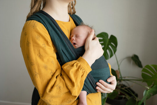 Crop woman standing with sleeping newborn in sling
